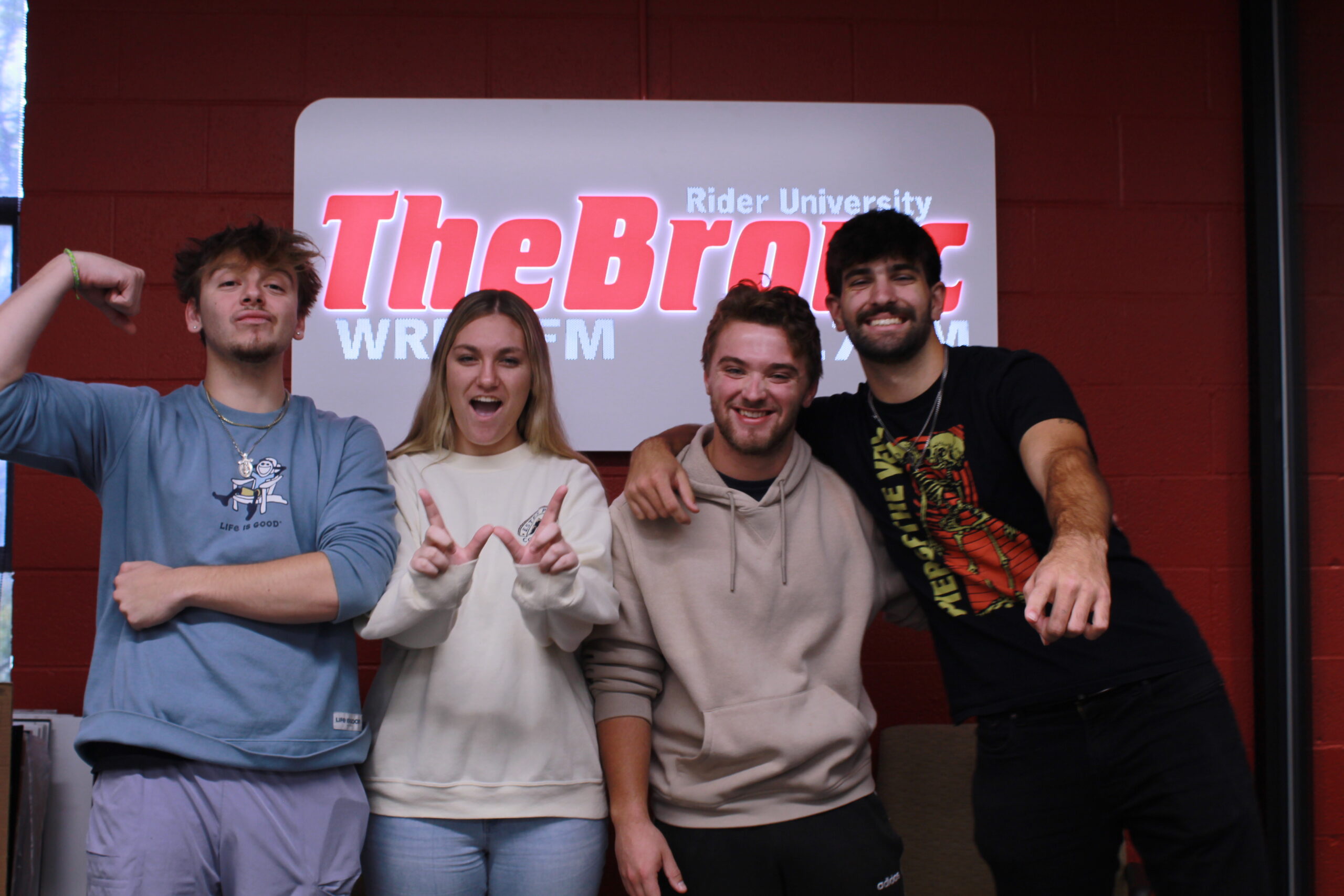 The Wake Up Rider Crew Nick, Alli, Jake, Owen, posing in front of the 107.7 The Bronc Sign
